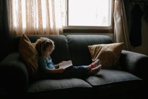 child reading on couch by window