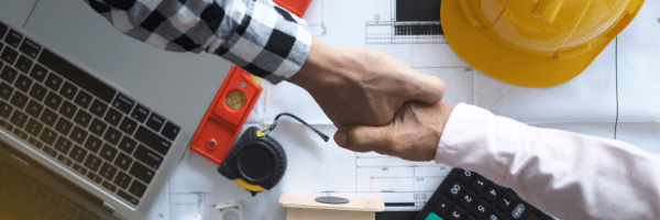 picture of two men shaking hands over what looks like house blueprints, a laptop, and some tools. safeguard your next project